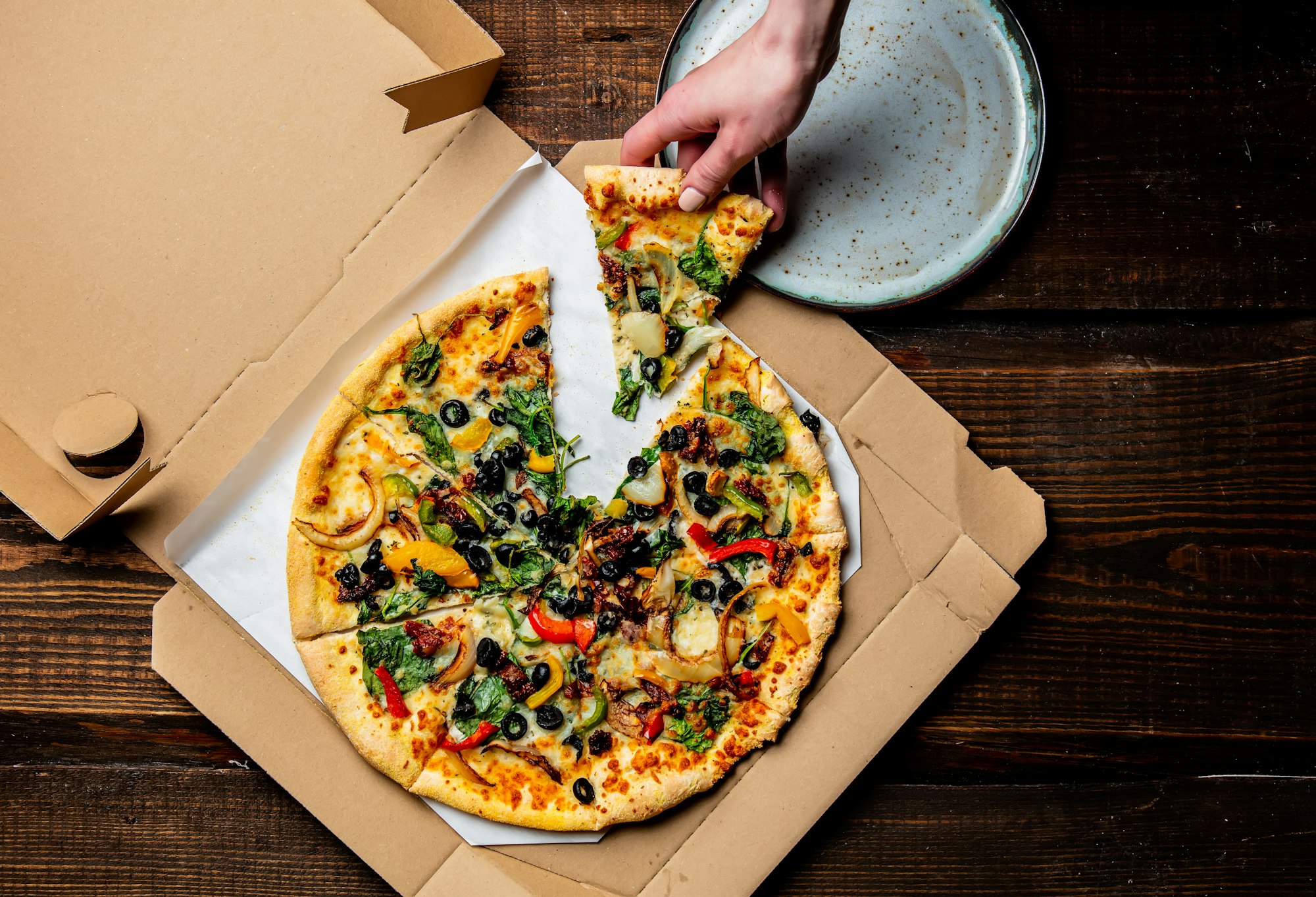 woman hand takes a mediterranean Pizza with olives and cheese from cardboard in a plate